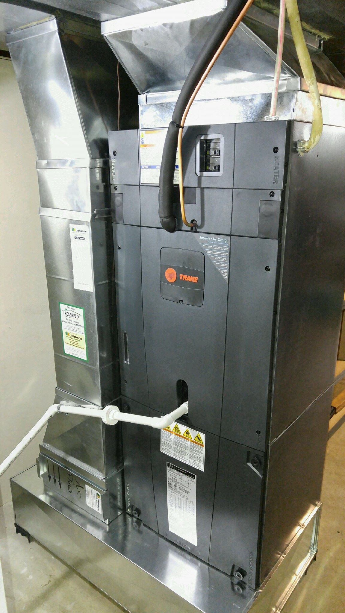A Trane Furnce with a hose attached to it is sitting in a room.