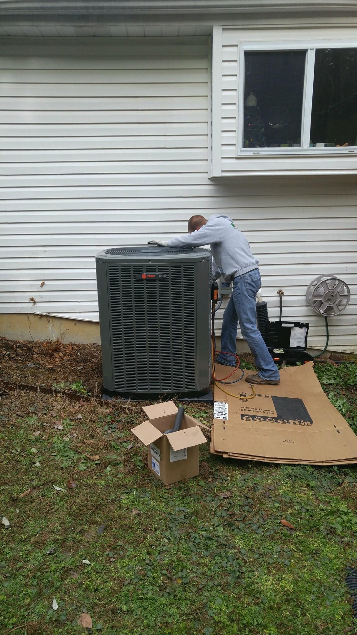 A man is working on an air conditioner outside of a house.