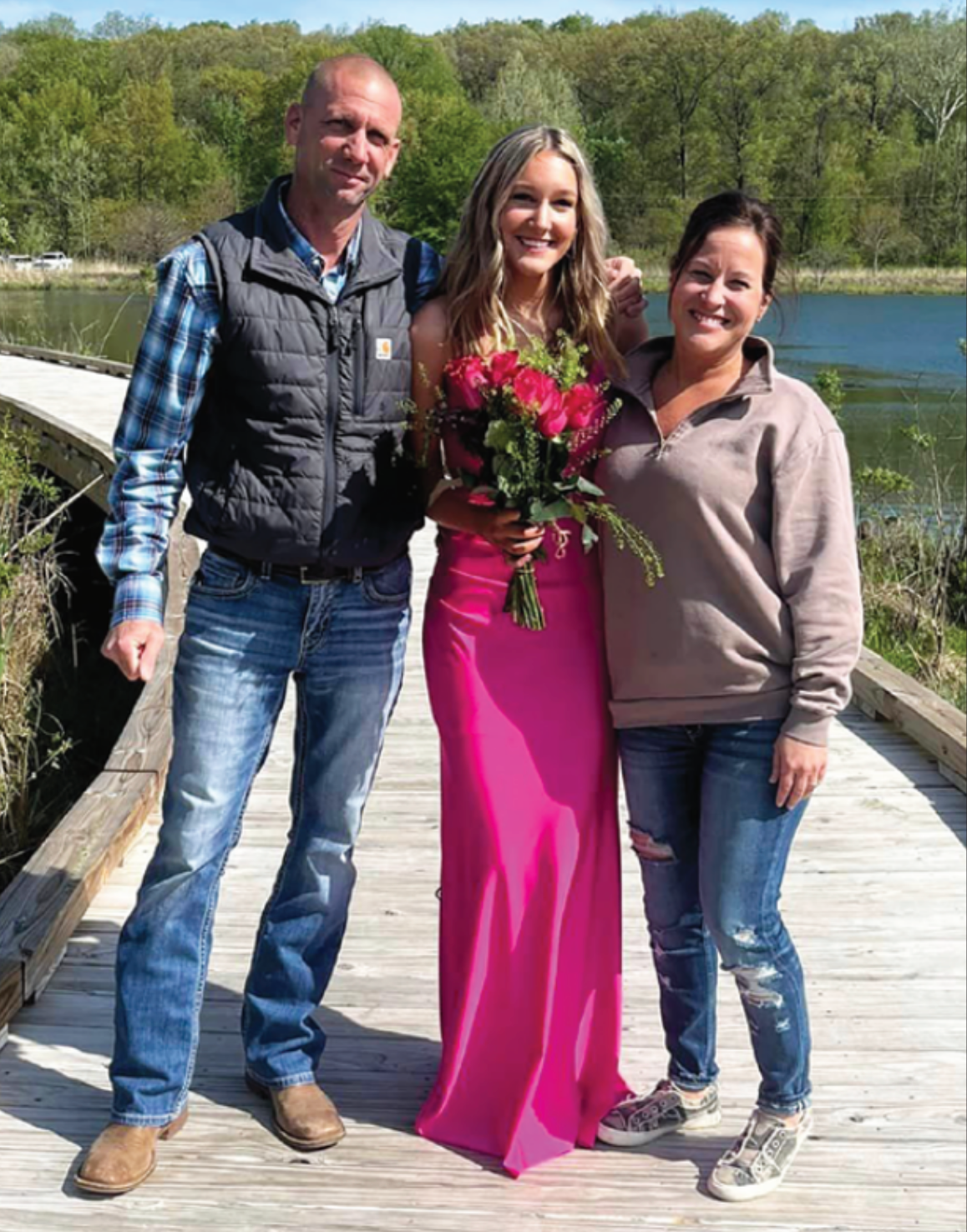 A man and two women are posing for a picture on a wooden bridge.