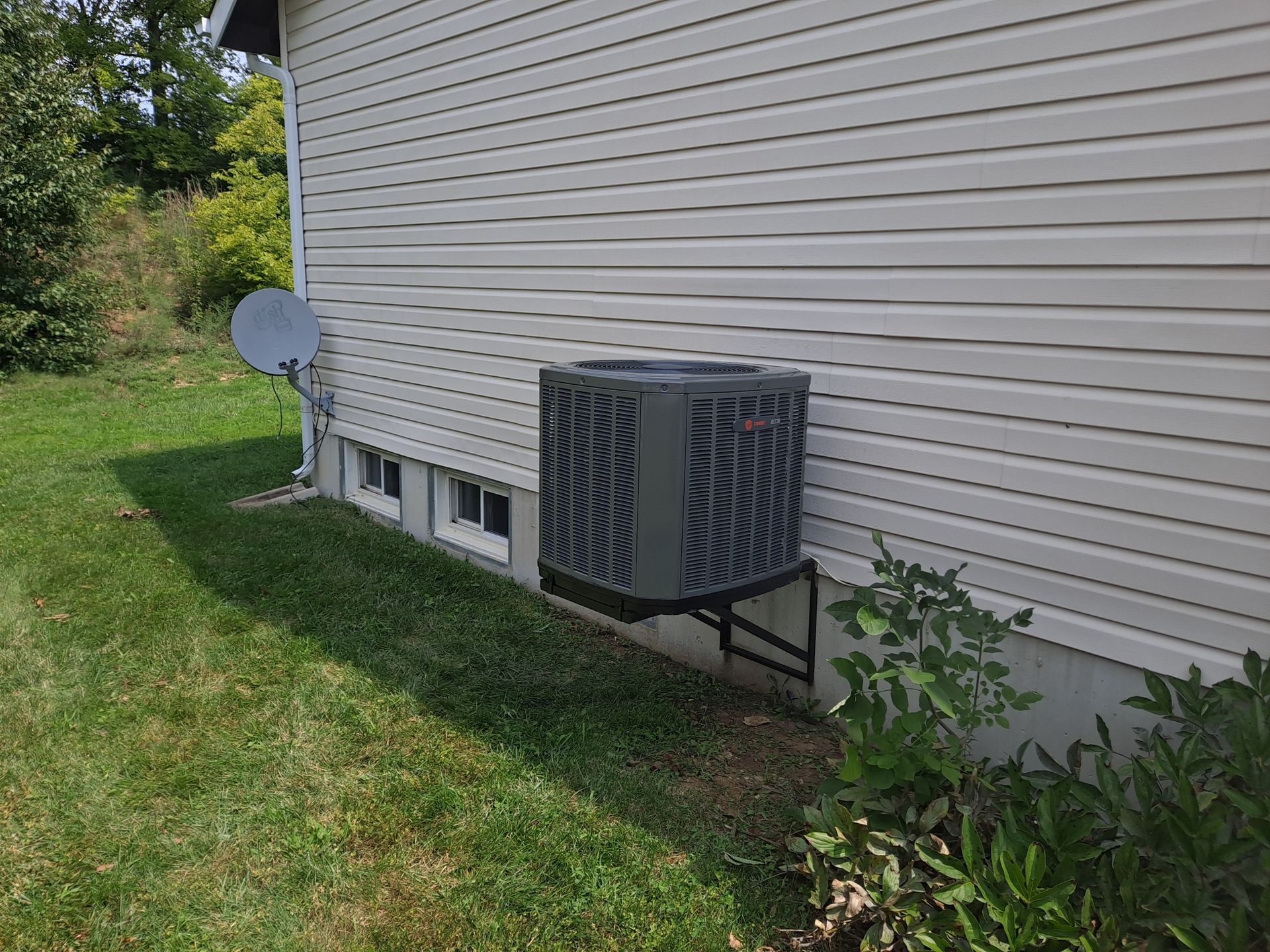An air conditioner is sitting on the side of a house next to a satellite dish.