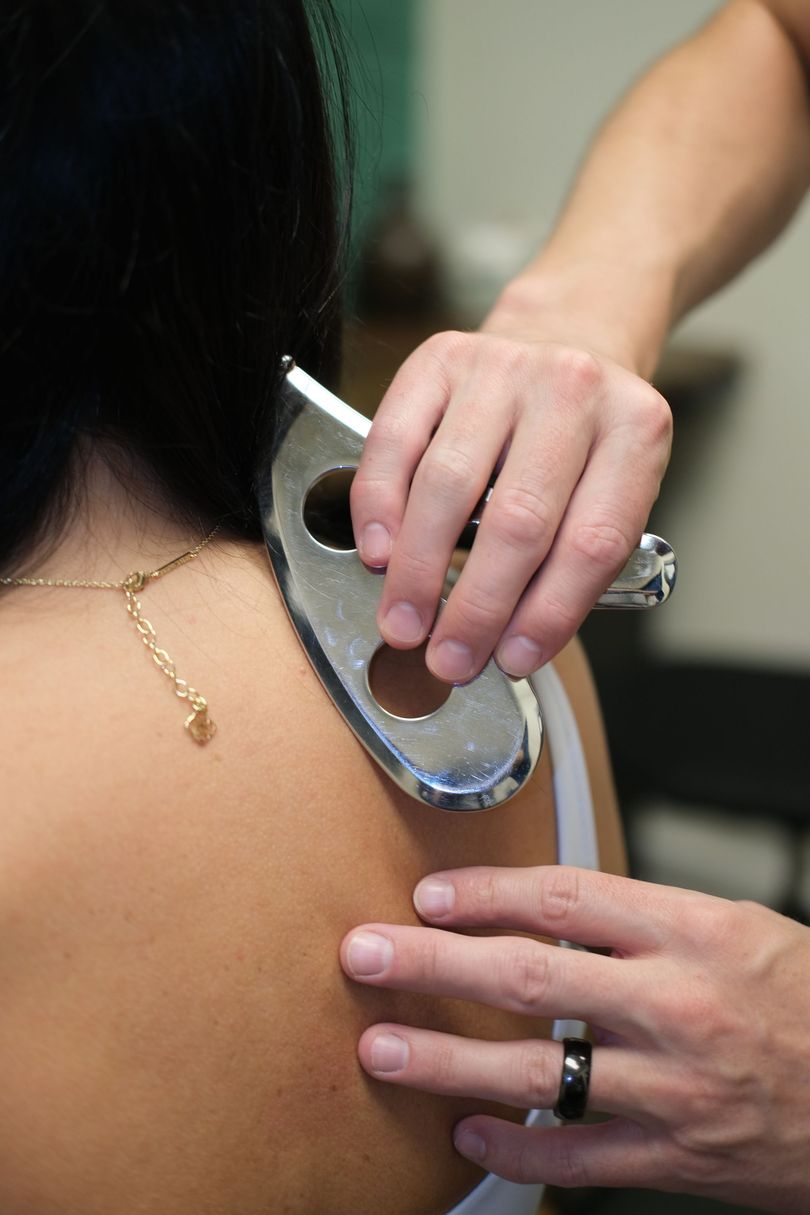 Hands using a handheld medical device on a person's upper back near the shoulder blade.