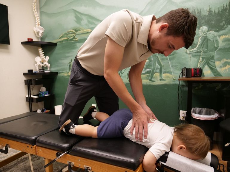 Chiropractor adjusting a patient on a treatment table in a clinic with green mural walls