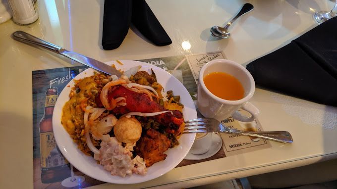 Plate of Indian food, small tea cup, knife, fork, and folded napkin on a table.