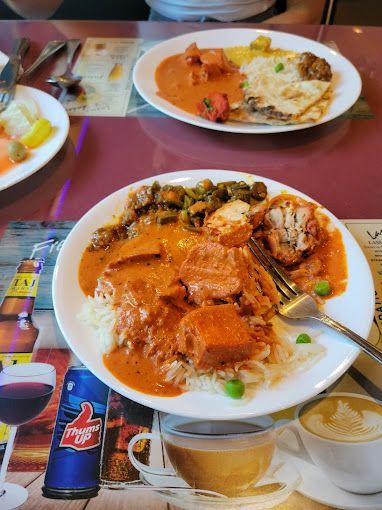 Plates of Indian food on a table: butter chicken, rice, vegetables, and naan.