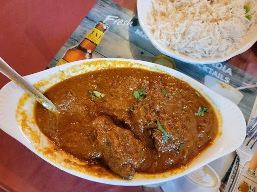 Close-up of a white oval dish filled with dark brown curry and garnished with cilantro, next to a bowl of white rice.