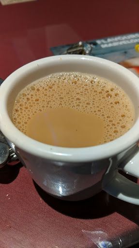 White mug filled with milky tea, on a red surface with a blur of other items in the background.
