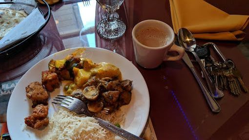 Plate of food with rice, curry, and fried items. Coffee cup and silverware on a table.