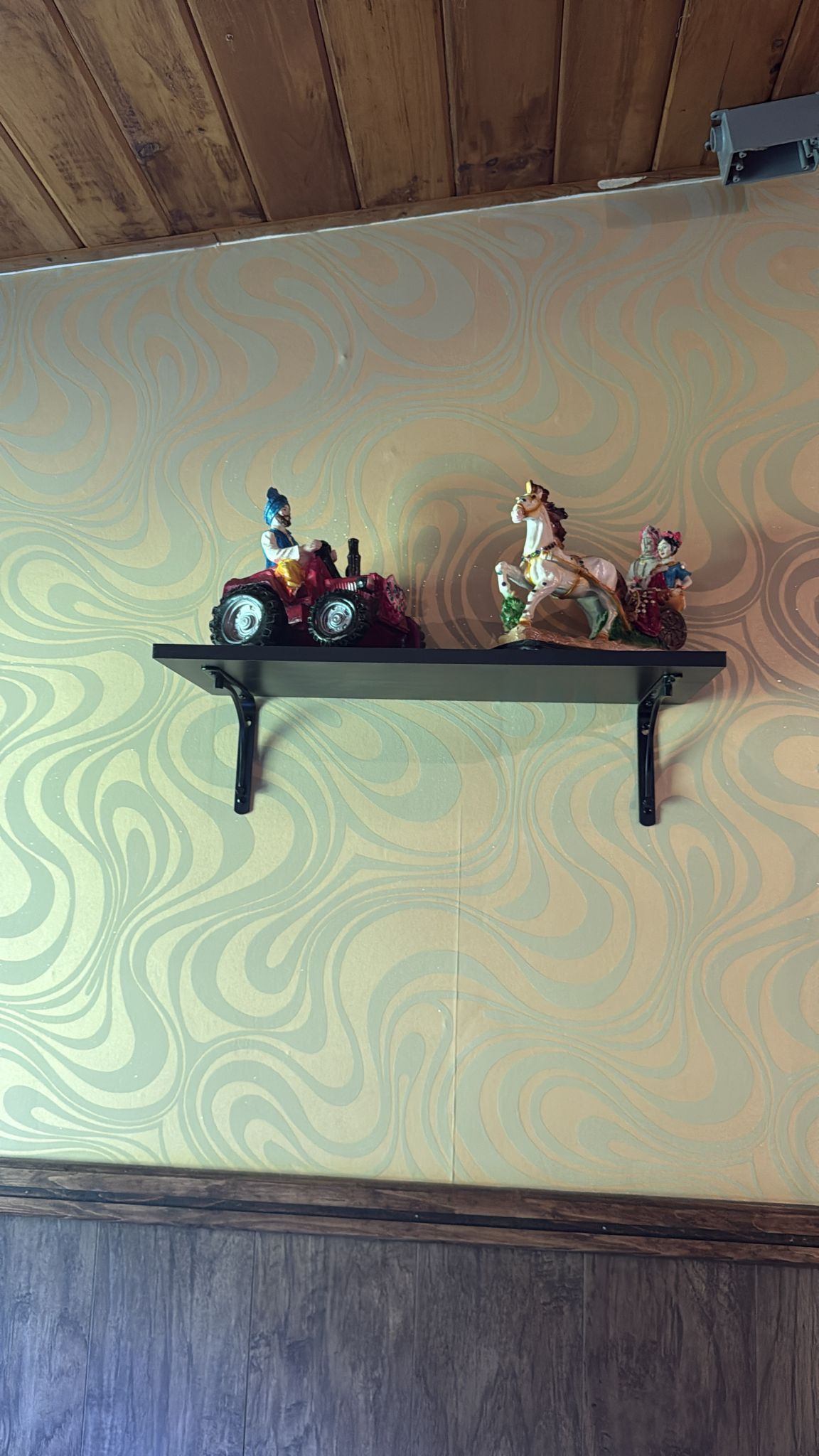 Shelf with toy tractor and ceramic figurines on wallpapered wall.