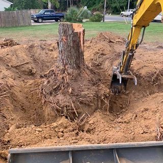 A yellow excavator is digging a hole in the ground next to a tree stump.