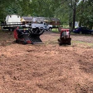 A bulldozer and a stump grinder are sitting in a dirt field.