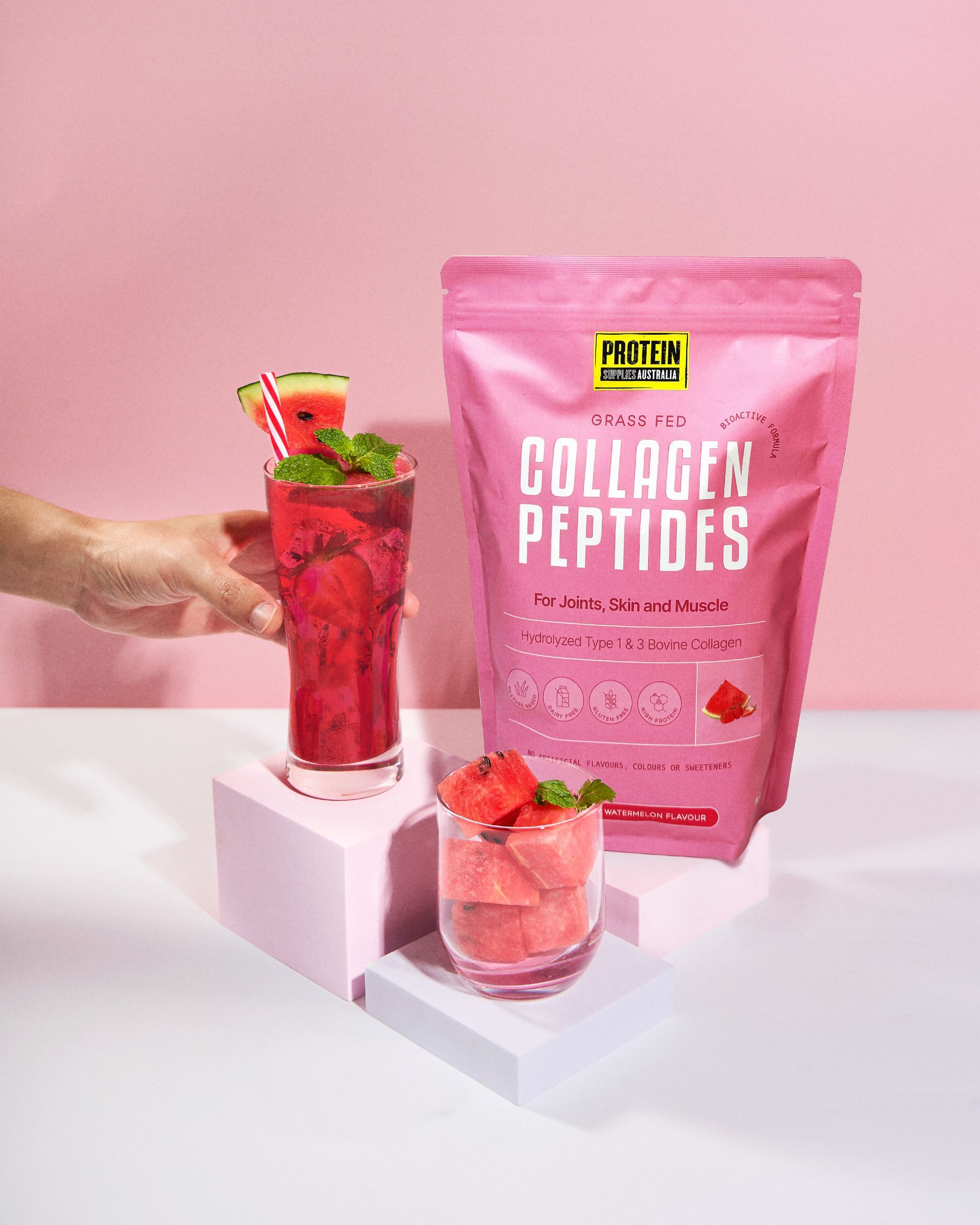 Pink bag of collagen peptides next to two watermelon drinks, one being held by a hand.