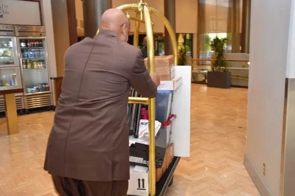 Person pushing a luggage cart through a hotel lobby, with a beverage cooler and wooden floors in the background