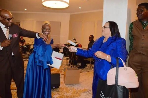 People exchanging gifts and handshakes at a formal indoor event, dressed in bright blue and dark suits