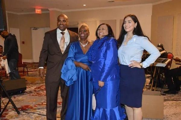 Four people in formal attire posing together at an indoor event with a band in the background