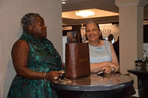 Two people stand at a round table in a lobby, smiling beside a brown gift bag.