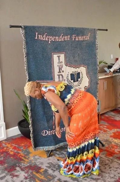Person in orange dress adjusting a memorial banner beside a floral display indoors