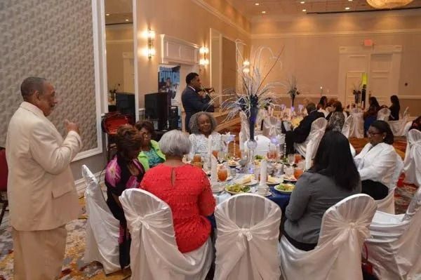 Formal banquet with seated guests at round tables and a speaker addressing the room