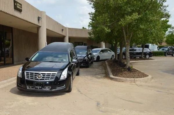 Black sedan parked by a tan office building, with several cars lined up along the curb.