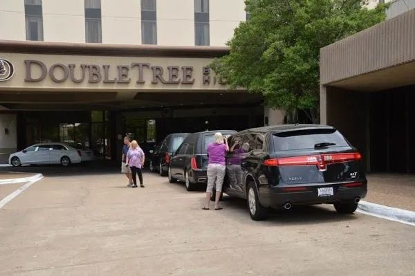 People loading luggage into black SUVs outside a DoubleTree hotel entrance