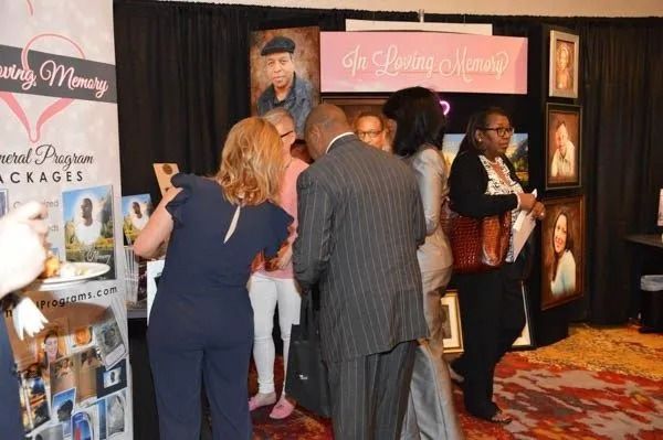 People browsing a vendor booth at an indoor event with posters and brochures on display