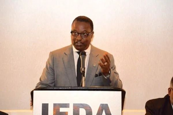 Speaker at a podium with JEDA sign, gesturing during a presentation