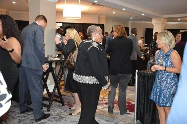People mingling at a formal indoor reception, chatting near cocktail tables.