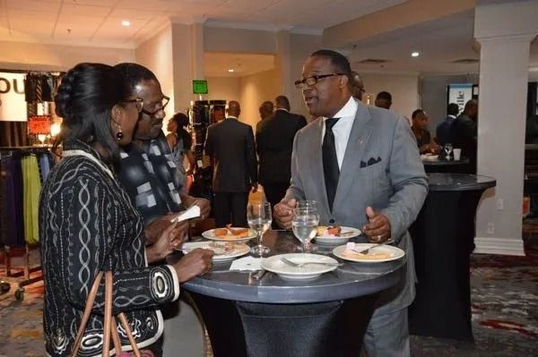 Three people converse at a cocktail table during a formal indoor reception.
