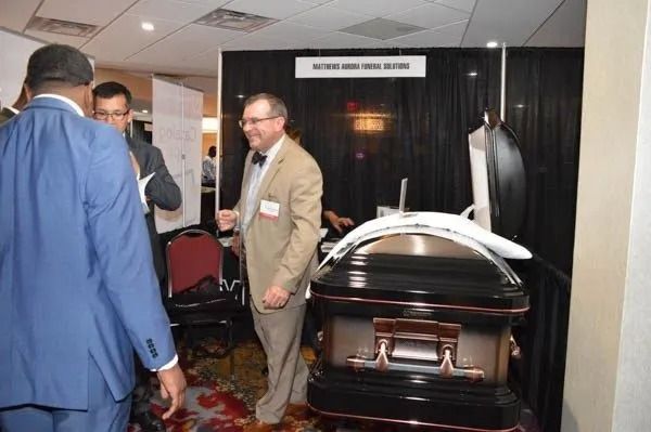 Men in suits at an indoor funeral expo beside a shiny black casket