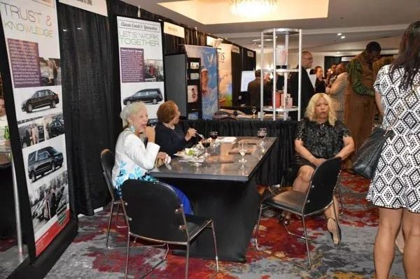 Booth display at a busy indoor event, with people seated and standing around a table in a conference hall.