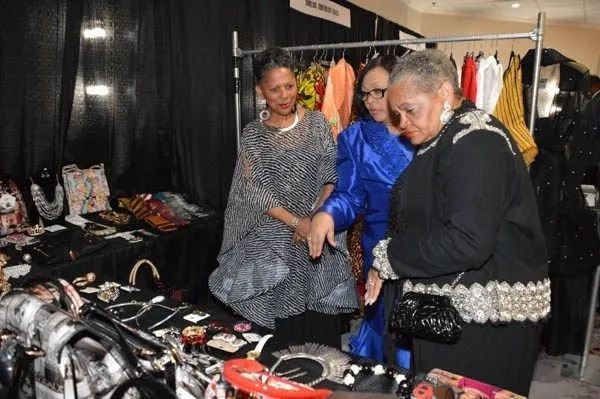 Three women browsing jewelry and clothing at a market stall