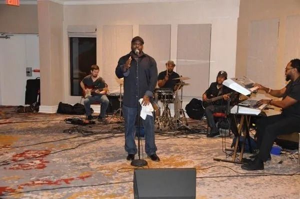 Band performing in a hotel ballroom, with singer at center and musicians seated around him.