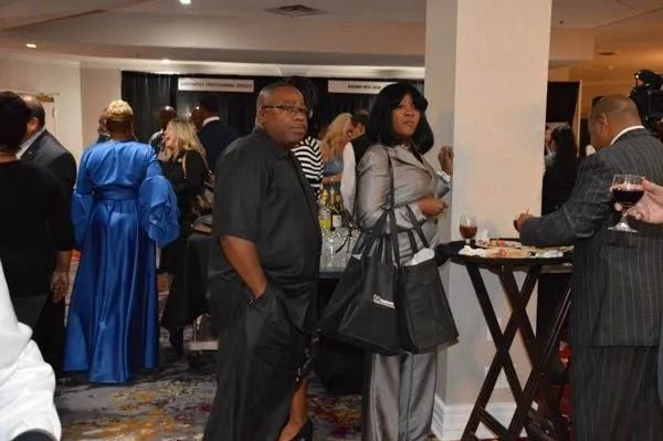 People mingling at a formal indoor event, with guests in blue and gray attire near a cocktail table.