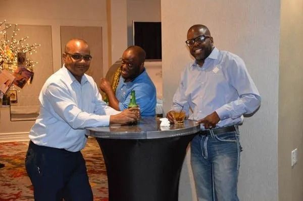 Three men in dress shirts chatting around a cocktail table at an indoor event.