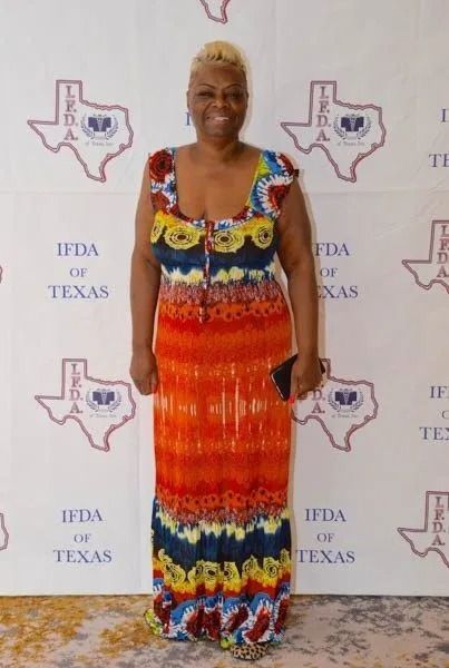 Person in a colorful dress standing in front of an IFDATexas backdrop at a formal event