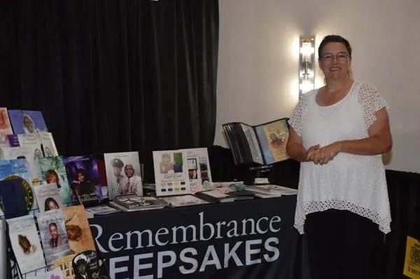 Woman standing beside a “Remembrance Keepsakes” display table with memorial items and photos
