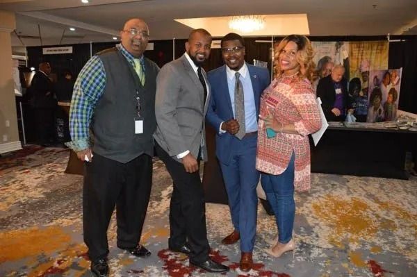 Four people posing together at a conference venue, dressed in business attire.