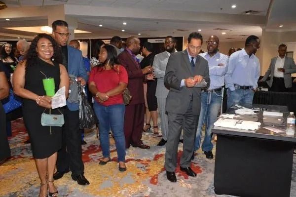 People standing in a conference lobby, some holding drinks and looking at phones near a buffet table