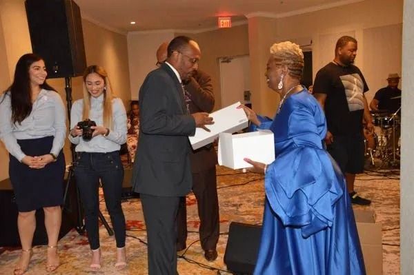 Woman in a bright blue gown receives an award from a man in a suit at a formal indoor event.
