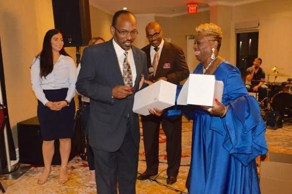 People holding open boxes at an indoor ceremony, with a woman in blue receiving an award