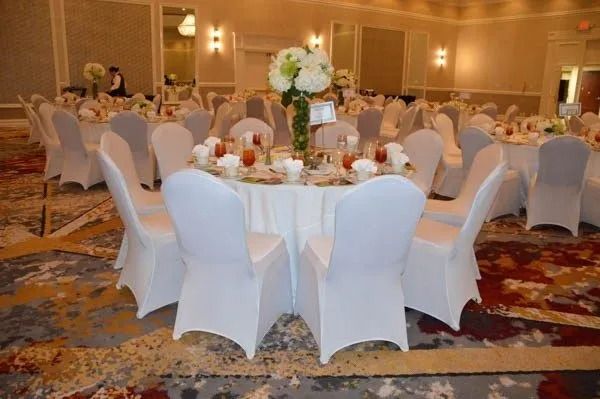 Round banquet tables with white chair covers in a warmly lit ballroom banquet hall