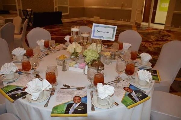 Round banquet table with white napkins, floral centerpiece, place cards, and mugs in a hotel ballroom.