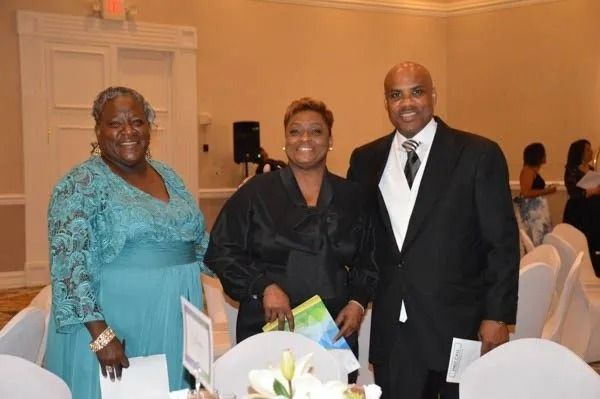 Three people pose smiling at a formal indoor event beside a white-clothed table.