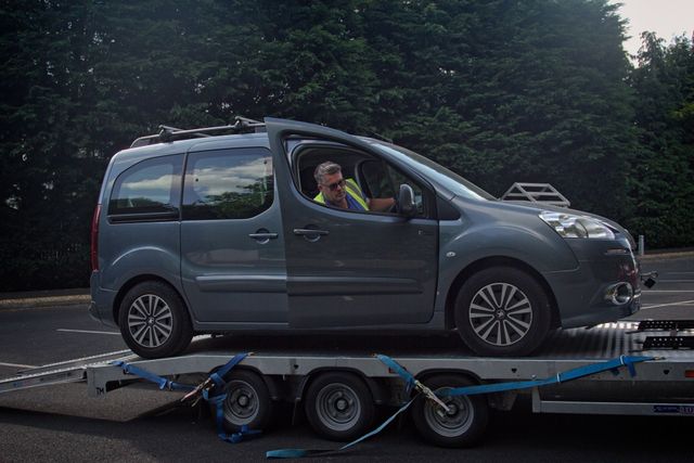 A man is loading a broken down car onto a 24hr recovery trailer.