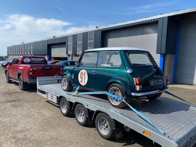 A green mini cooper classic car on a vehicle transportation trailer being transported from Ballymarlagh.