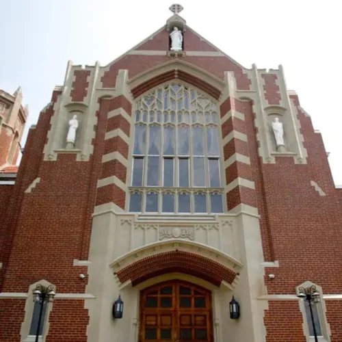 Red brick church facade with large arched stained-glass window and wooden entrance doors