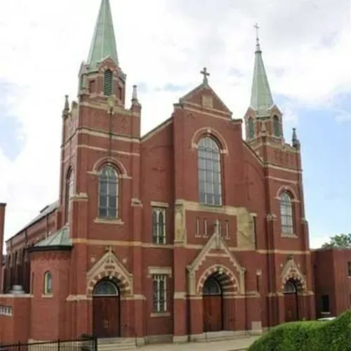 Red-brick church with tall green spires and arched windows on a cloudy day