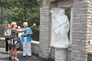 People standing beside a white statue in a stone monument display outdoors.