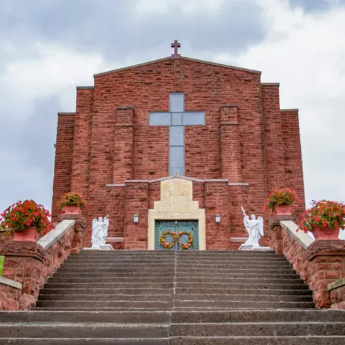 Red brick church facade with a large blue cross and stairs leading up to the entrance