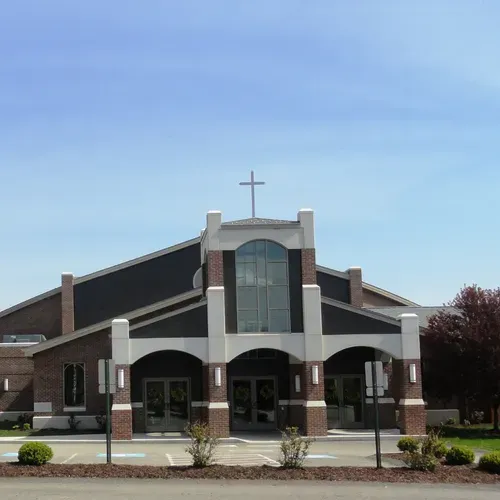 Church building with a cross, arched entrance, and brown-and-white facade under a blue sky