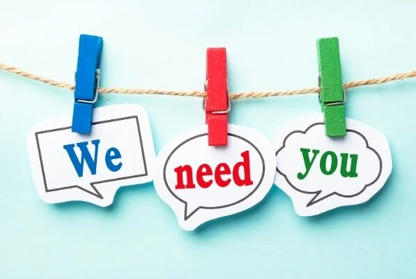 Clothespins hold cutout signs reading “We need you” on a string